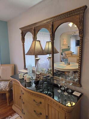Um quarto com um espelho grande e ornamentado, uma cômoda com copos e uma cadeira.