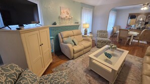 A living room with a TV, two sofas, a patterned armchair, a coffee table, and a dining area with chairs and a table. - Charming Fruitland Park Getaway (Fruitland Park)