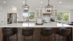 A modern kitchen with a large island, bar stools, stainless steel appliances, and a view of the outdoors. - WOW! Luxury Wine Country Estate - 6 Bedrooms • Hot Tub • Game Room (Temecula)