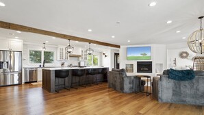 A modern kitchen with a central island, bar stools, and a large island bar. There is a fireplace, a TV mounted on the wall, and a chandelier. - WOW! Luxury Wine Country Estate - 6 Bedrooms • Hot Tub • Game Room (Temecula)