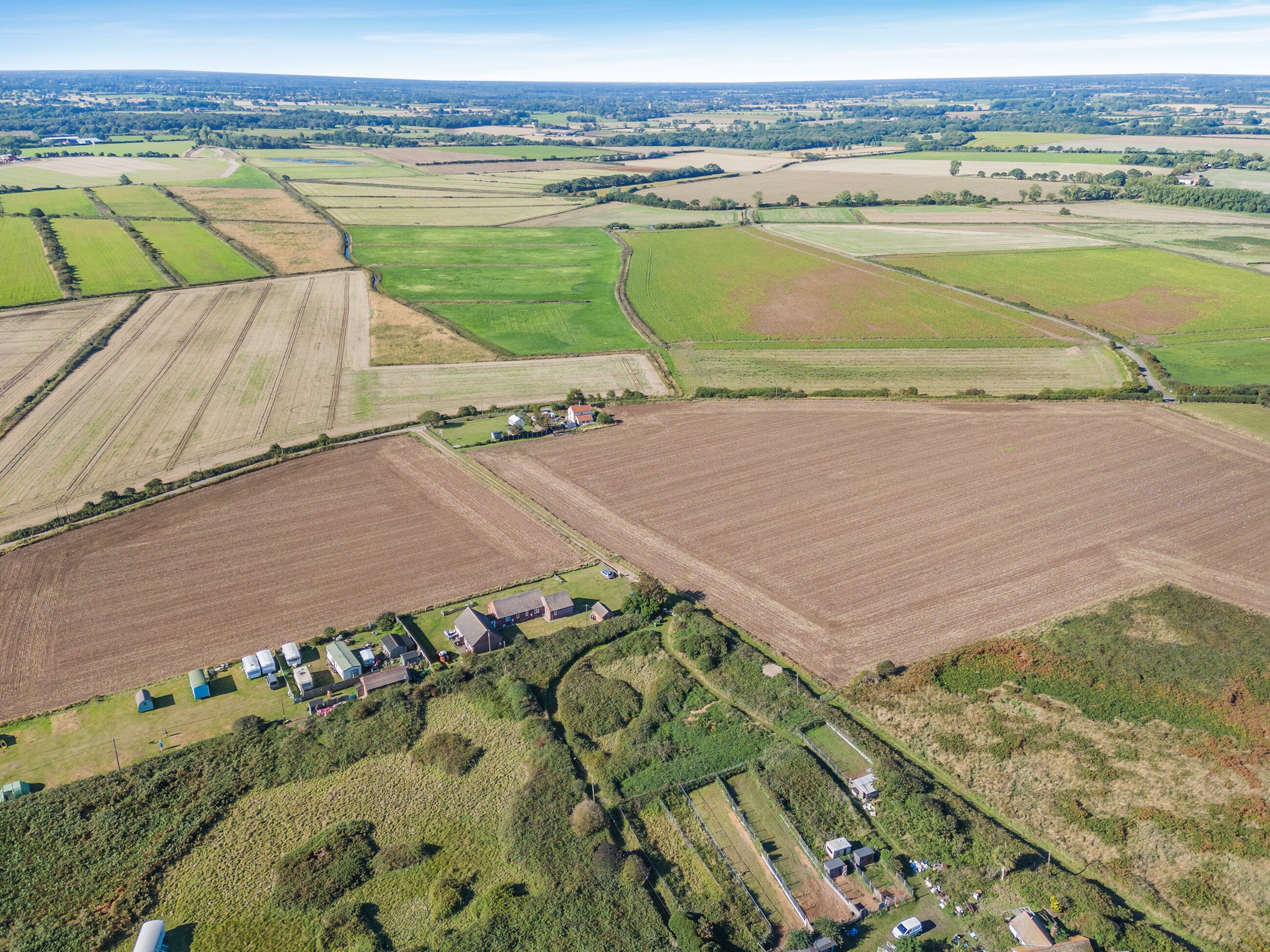An aerial view of a rural landscape with fields, a small cluster of buildings, and a road.