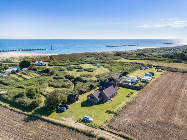 An aerial view of a coastal area with houses, a beach, and a rocky breakwater.