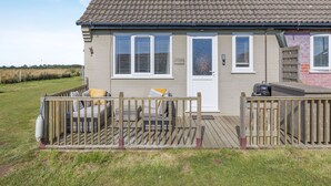 A single-story house with a tiled roof, a front porch with a wooden railing, and a small deck area. - 1 bedroom accommodation in Happisburgh (Happisburgh)