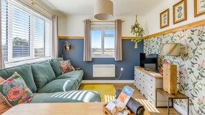 A modern living room with a green sofa, a wooden coffee table, a TV, and a plant. - 1 bedroom accommodation in Happisburgh (Happisburgh)
