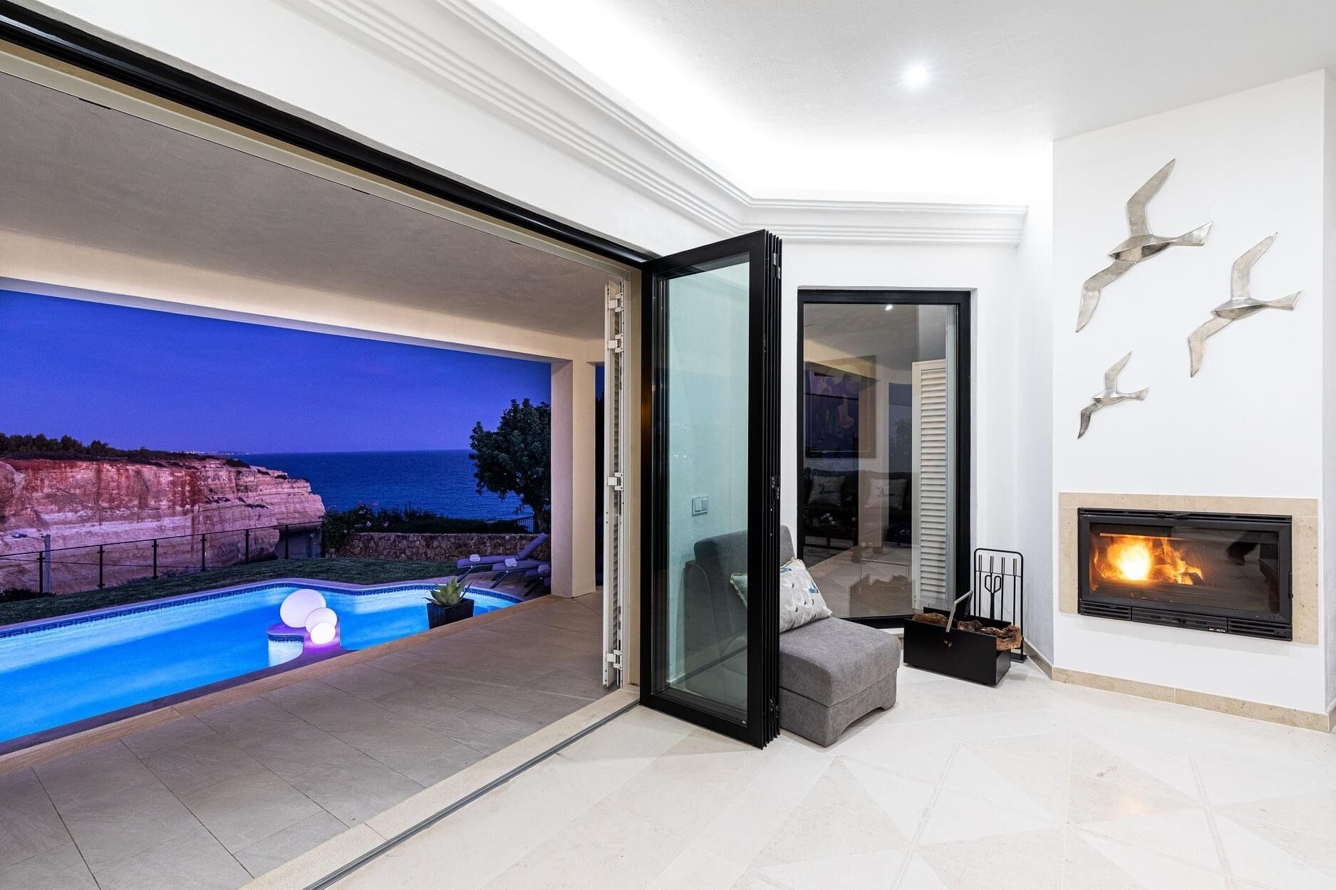 A modern living room with a large panoramic window, a fireplace, and a pool.