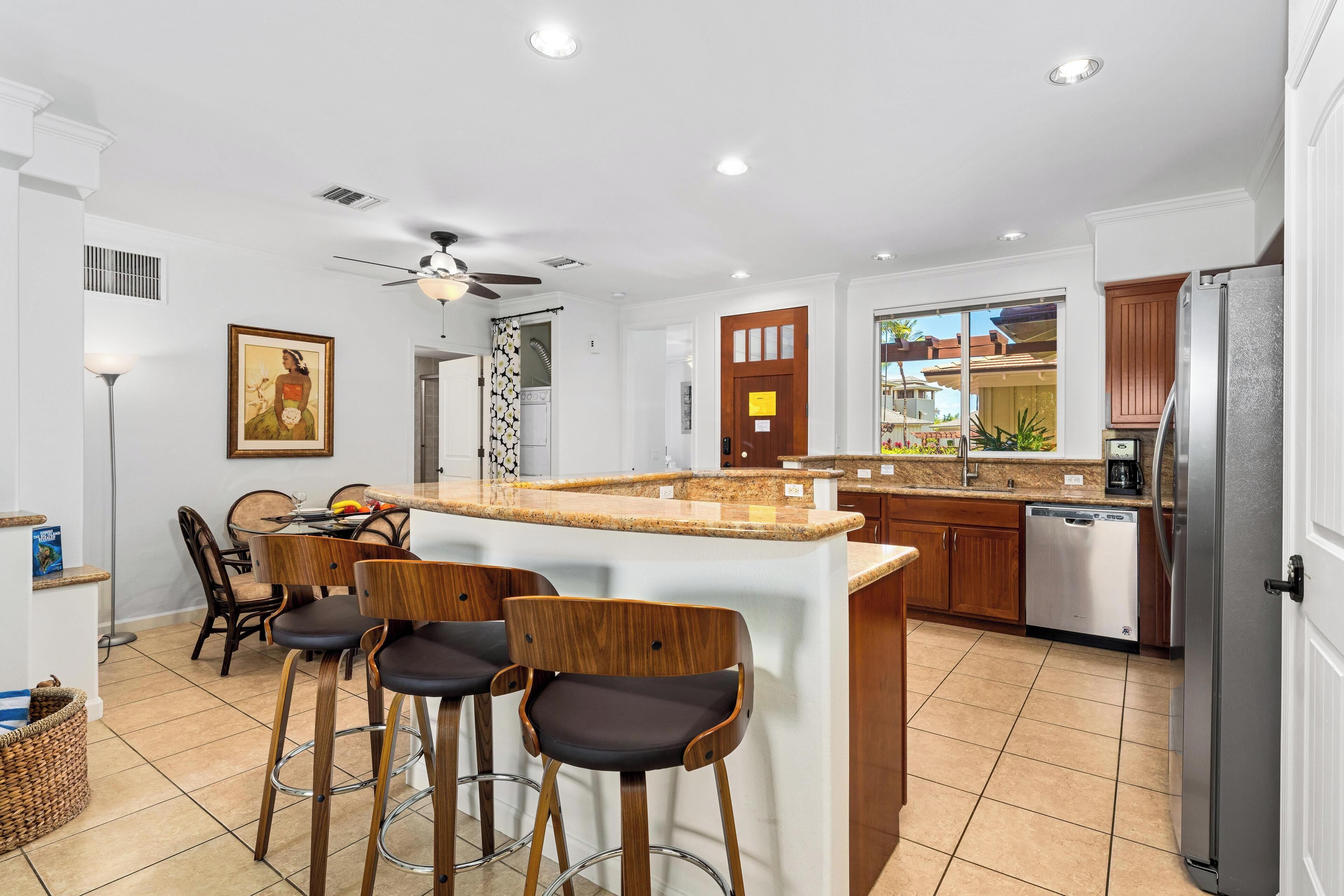 A modern kitchen with a central island, bar stools, a dining area with chairs, and a refrigerator.