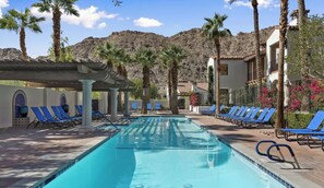 A swimming pool with lounge chairs, palm trees, and a mountainous backdrop.
