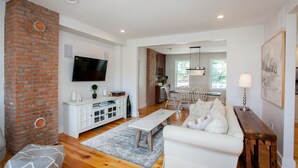 A spacious living area with a white sofa, a wooden coffee table, and a brick accent wall. - Main Street Livin’ (Flemington)