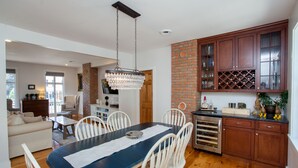 A modern kitchen with wooden cabinets, a wine rack, and a dining area with a table and chairs. - Main Street Livin’ (Flemington)