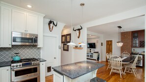 A modern kitchen with stainless steel appliances, a granite countertop, and a dining area with wooden chairs. - Main Street Livin’ (Flemington)