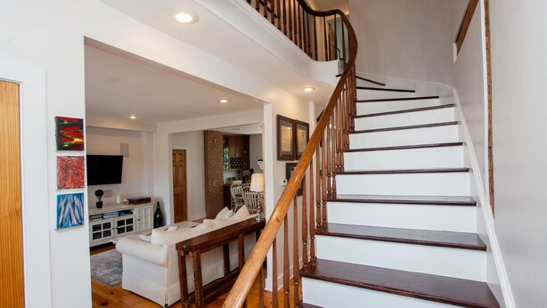 A staircase with wooden handrails leading to an upper floor. A white sofa and a dining table are visible in the lower level. - Main Street Livin’ (Flemington)