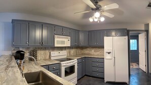 Une cuisine avec des meubles de couleur grise, un réfrigérateur blanc, un four à micro-ondes, une cuisinière et un évier.