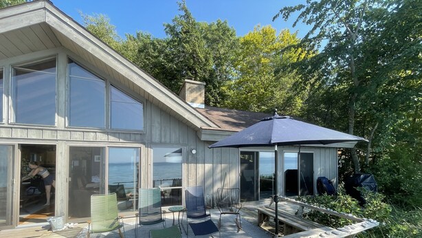 Ein modernes Haus mit großen Glasfenstern, einer Terrasse und Gartenmöbeln.