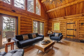 L’intérieur d’une cabane en rondins, avec deux canapés, une table basse et une grande porte en bois.