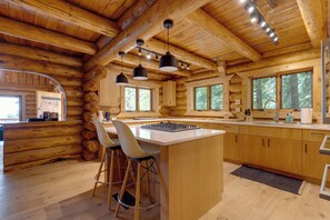 L’intérieur d’une cabane en rondins, avec un îlot de cuisine, des tabourets de bar, des armoires en bois et des luminaires suspendus.