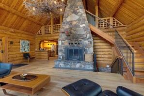 L’intérieur d’une cabane en rondins, avec une cheminée en pierre, un escalier en bois et un coin repas.