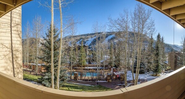 A view through a circular window of a building with a mountain in the background, trees, and a clear sky.