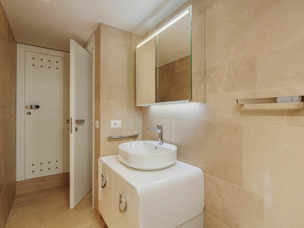 Ein Badezimmer mit einem weißen Waschbecken, einem Spiegel und beige gefliesten Wänden.