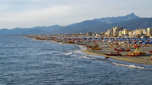 A coastal beach with numerous umbrellas and boats, a clear sky, and mountains in the background. - Cosy apartment for 7 people with WIFI, A/C, TV and patio (Viareggio)
