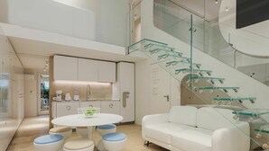 A modern interior with a white sofa, round table, and stools, a kitchen area, and a glass staircase. - Cosy apartment for 7 people with WIFI, A/C, TV and patio (Viareggio)