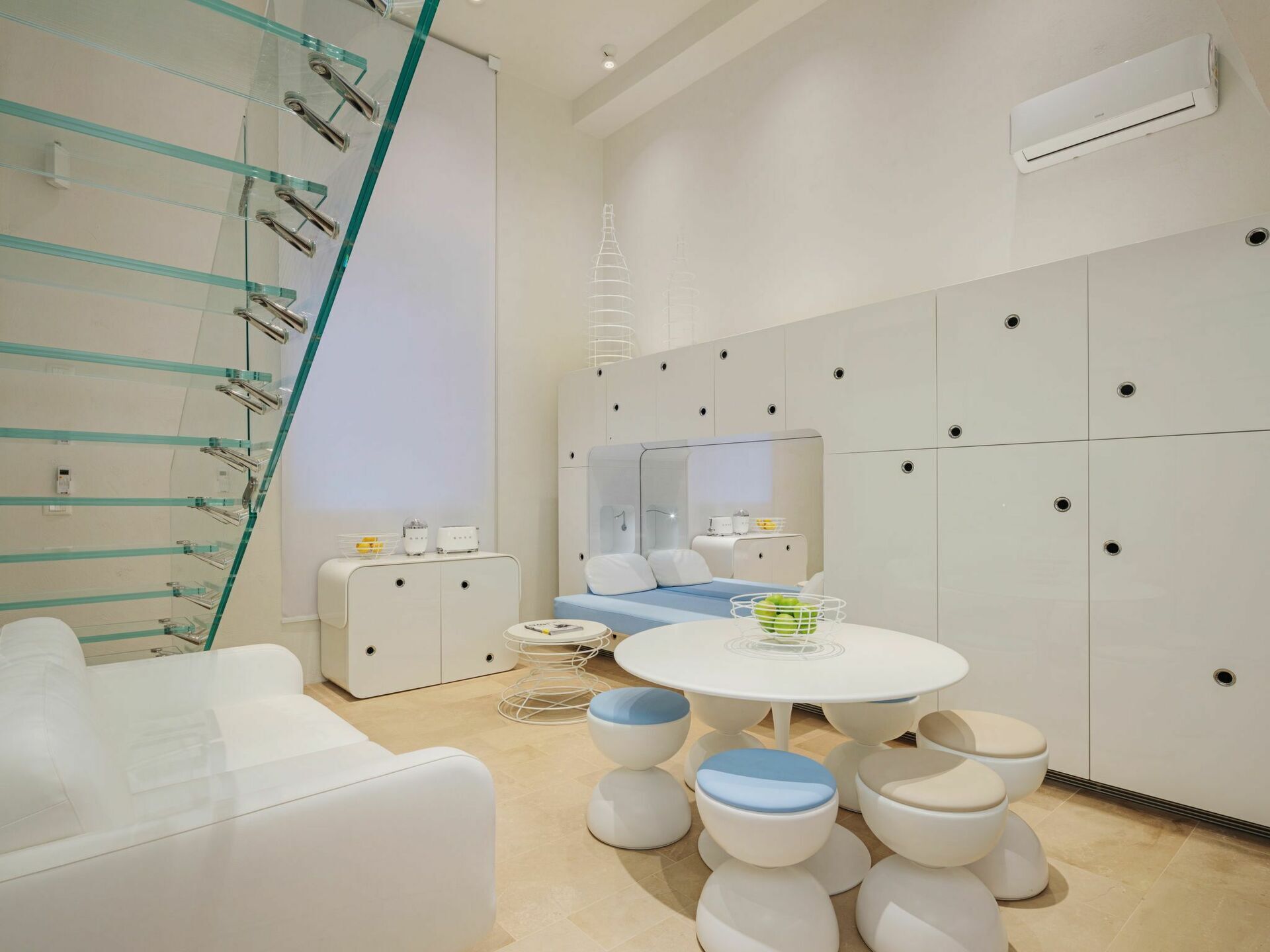 A modern bathroom with a glass shower enclosure, a round white table with stools, and a mirrored cabinet.