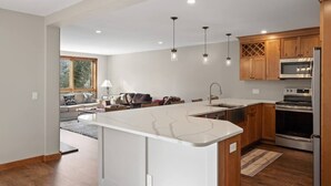 A modern kitchen with a central island, wooden cabinets, stainless steel appliances, pendant lighting, and a view into the living area. - Spacious 3 Level 3BR+3Bath Townhouse w/Fireplace (Dover)