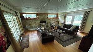 A living room with a stone fireplace, leather sofas, wooden flooring, and large windows.