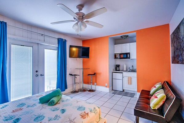 Een slaapkamer met een bed, een plafondventilator, een televisie, een kitchenette en een badkamer.