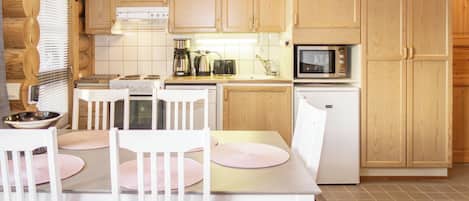 A wooden cabin kitchen with a dining table, chairs, a stove, a microwave, and a refrigerator.