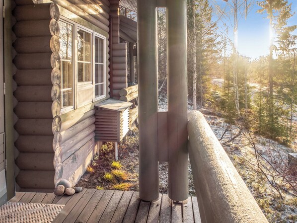 A log cabin with a porch, a window, and a view of a forested area.