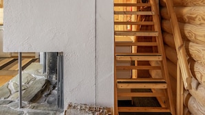 A staircase with wooden steps and a metal railing, leading to a room with a stone fireplace and a white textured wall.