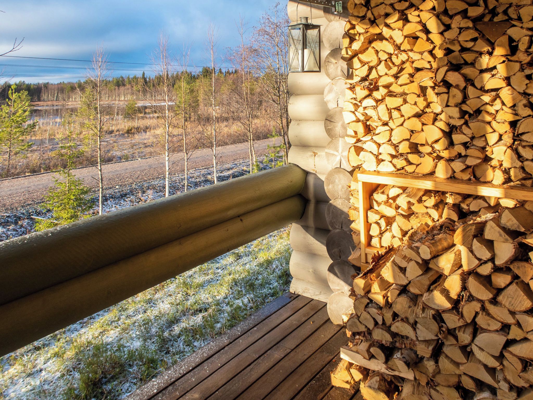 A wooden deck with a railing, a stack of firewood, and a view of a forested area.