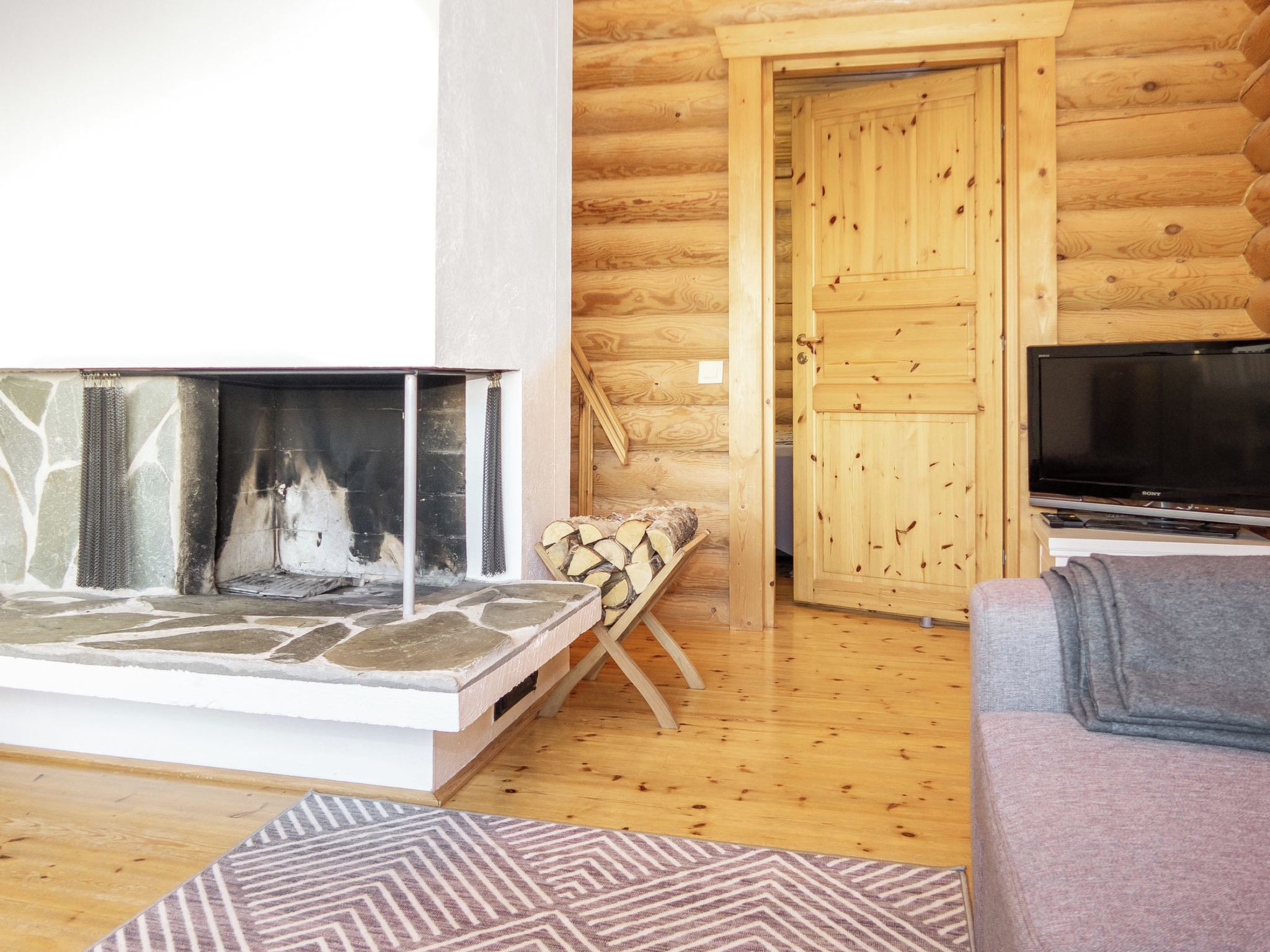 Un salon chaleureux avec une cheminée en pierre, un téléviseur et une porte en bois.
