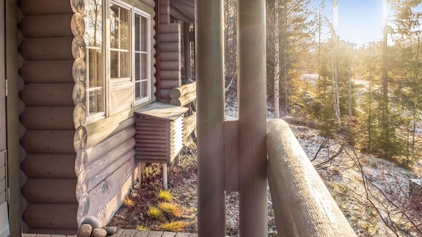 A log cabin with a wooden deck and a window overlooking a forested area.