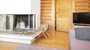 A log cabin interior with a stone fireplace, a television, and a wooden staircase.
