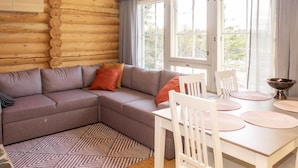 A cozy log cabin interior with a gray sectional sofa, white dining table, and chairs.