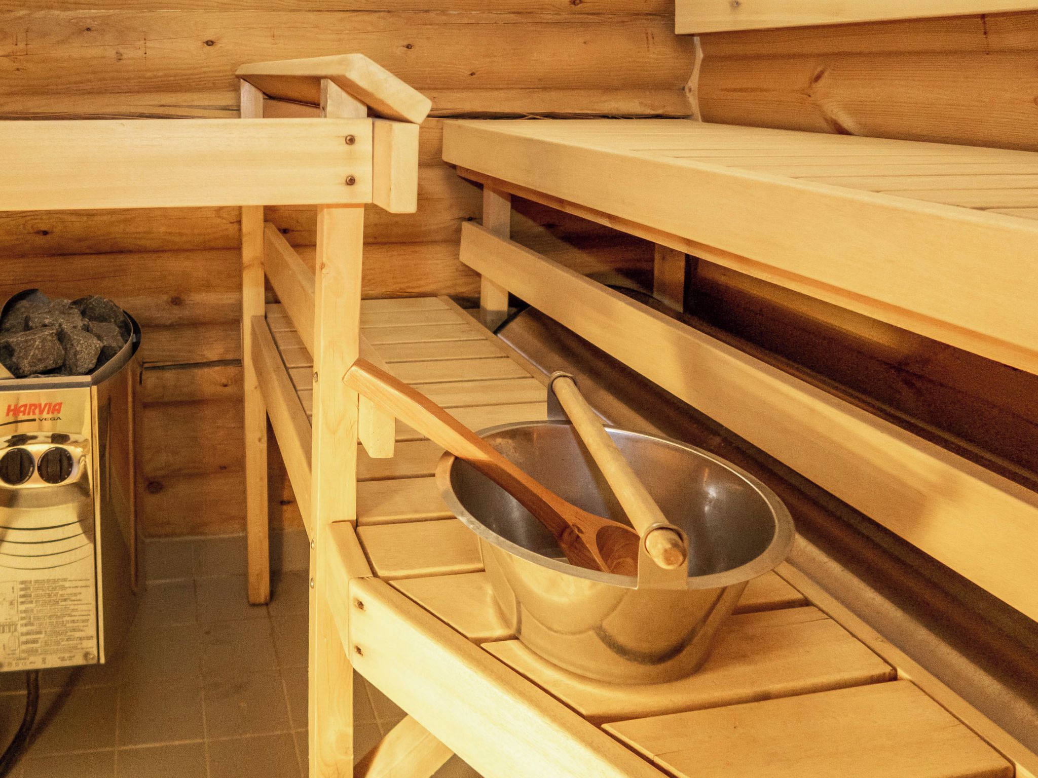 Una sauna con panche in legno, uno scaldasalviette e una bacinella di metallo con una paletta in legno.