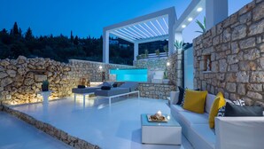 A modern outdoor living area with a stone wall, a pool, and a white pergola. - Dion Villa - Pool & Jacuzzi - Sleeps 4 - Zakynthos (Zakynthos)