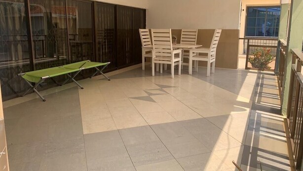 Un balcón amplio con una mesa plegable verde, sillas blancas y vistas al exterior.