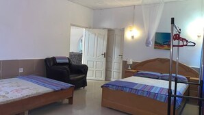 Una habitación con dos camas individuales, una silla, un ventilador de techo y una puerta que da a otra habitación.