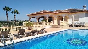A pool with lounge chairs, a building with arches, and palm trees in the background. - Villa - Sleeps 7 - Pool - Parking (Javea)