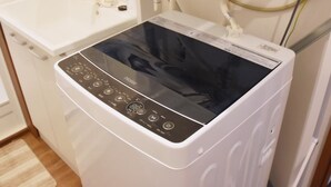 Eine moderne, kompakte Waschmaschine mit digitaler Steuerung in einem Hotelzimmer, mit Waschbecken in Weiß und Holzboden.