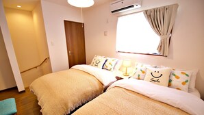 Ein Hotelzimmer mit zwei Betten, einem Fenster mit Vorhängen, einer Holztür und einer Klimaanlage.