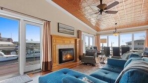 Un amplio salón con chimenea, ventanas grandes y vistas a barcos y edificios.