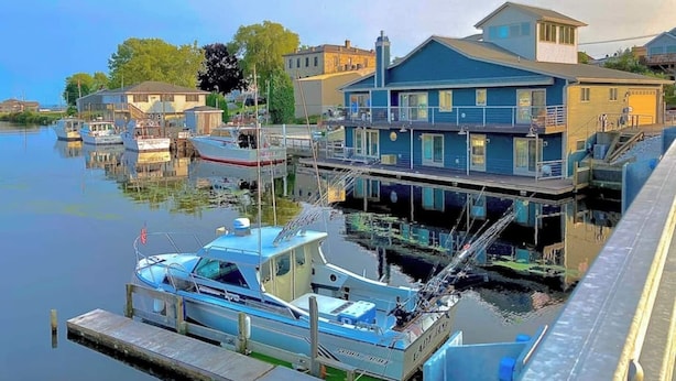 Una propiedad frente al agua con un muelle, un bote y una casa con balcón con vista al agua.