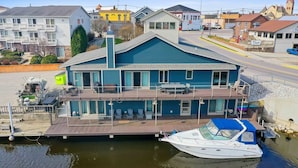 Una propiedad frente al agua con un muelle, un bote, y un edificio con varios balcones y una terraza cubierta.