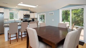 A modern kitchen with white cabinets, a microwave, and a dining area with a large wooden table and chairs.