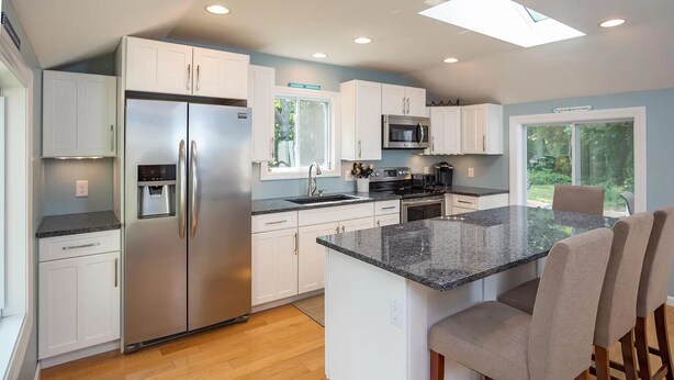 A modern kitchen with white cabinets, stainless steel appliances, a granite countertop, and a dining area with a bench.