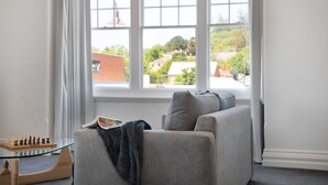 A living room with a grey sofa, a glass coffee table with a chess set, and a view of a residential area through large windows. - 1913 on Vincent Soaring ceilings and stunning Views (Daylesford)
