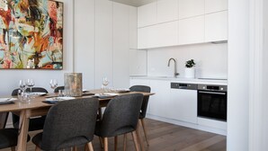 A modern kitchen with white cabinetry, a dining area with a wooden table and grey chairs, and a large abstract painting on the wall. - 1913 on Vincent Soaring ceilings and stunning Views (Daylesford)